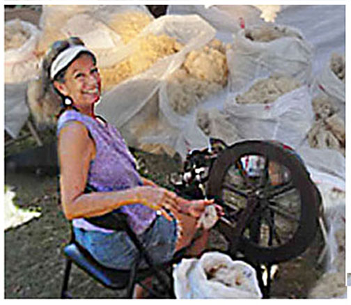 Alice at spinning wheel with bags of wool