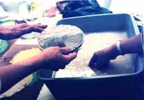 Paper-making, hands screening pulp from a tub.
